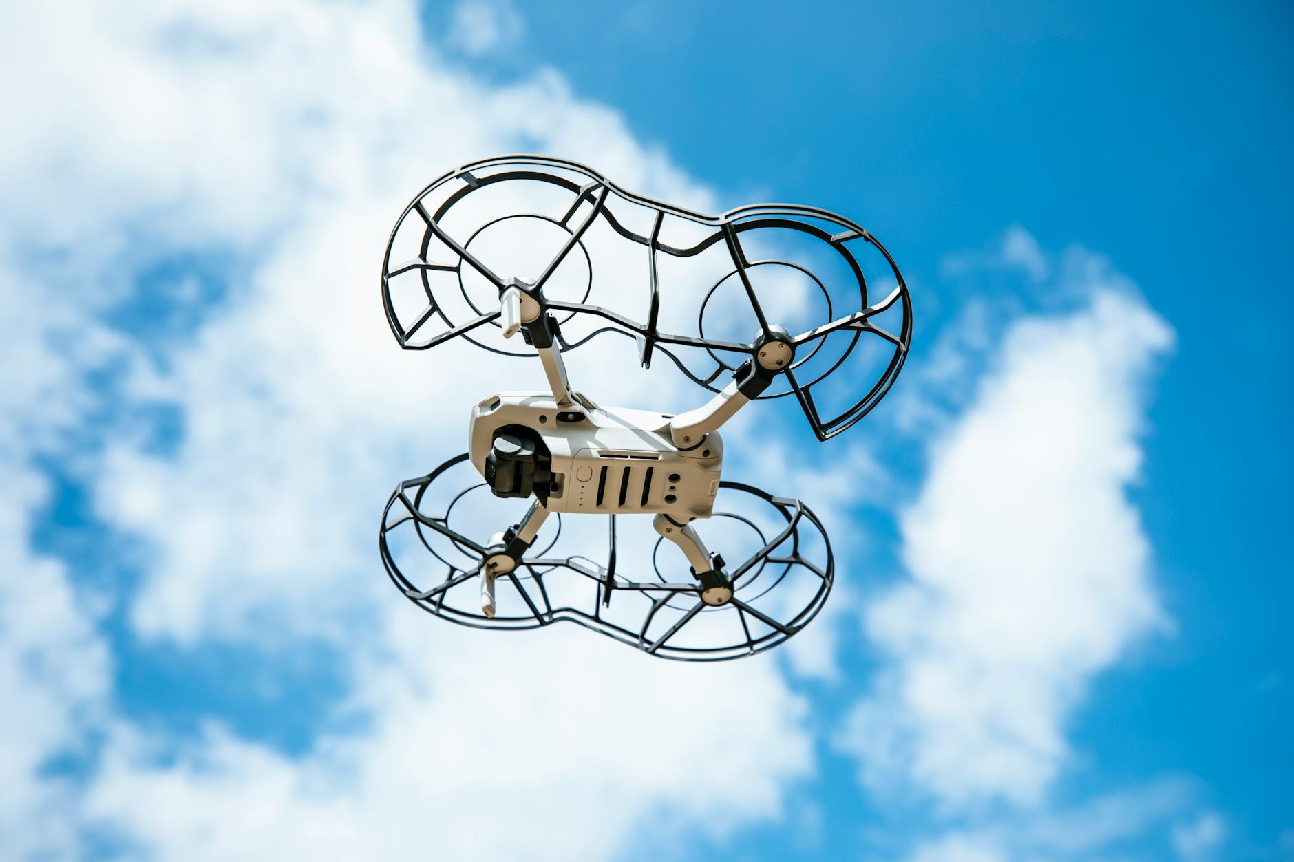 A close-up view of a drone flying against a bright blue sky with white clouds.