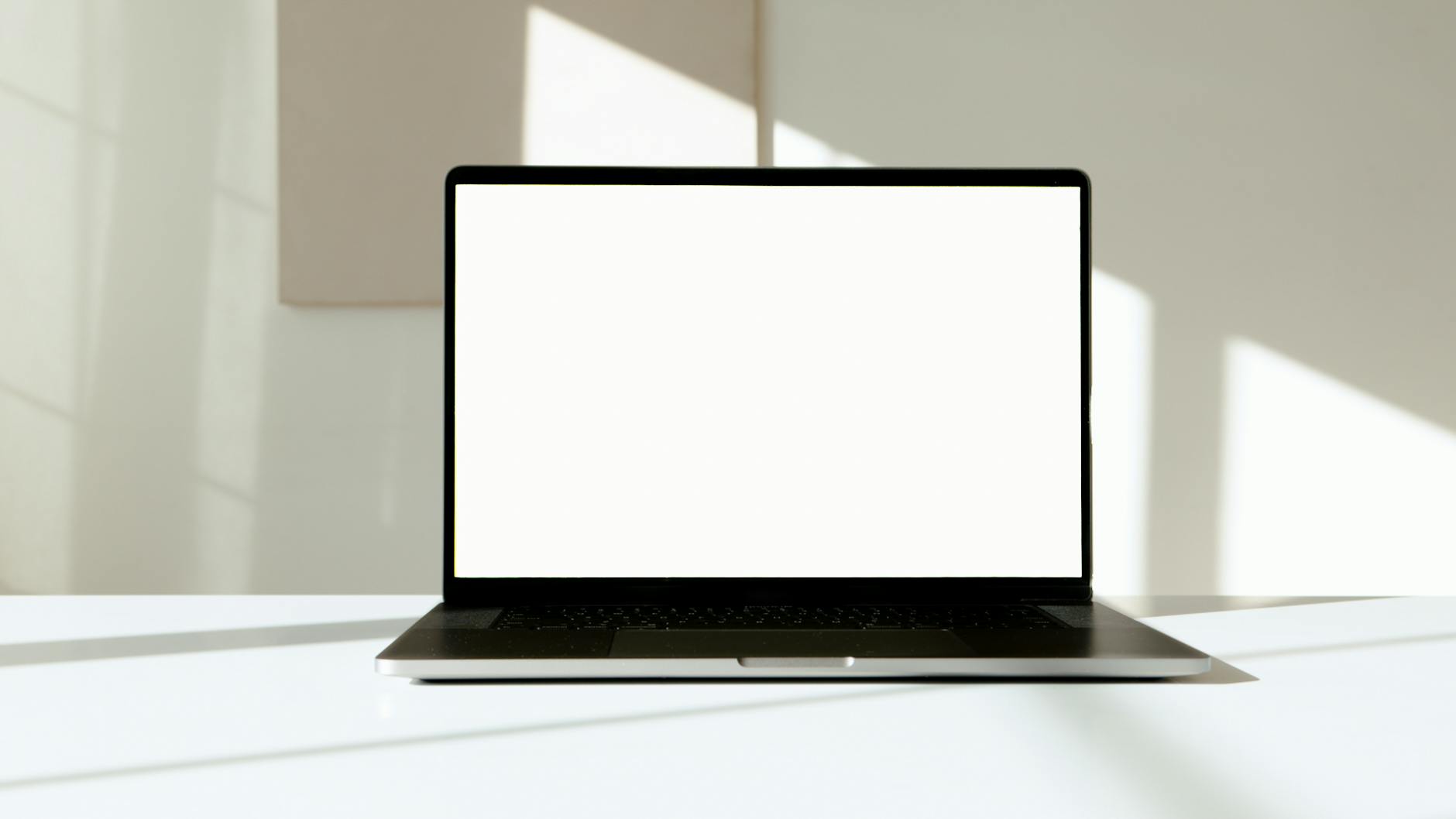 A laptop with a blank white screen on a desk, bathed in natural sunlight.