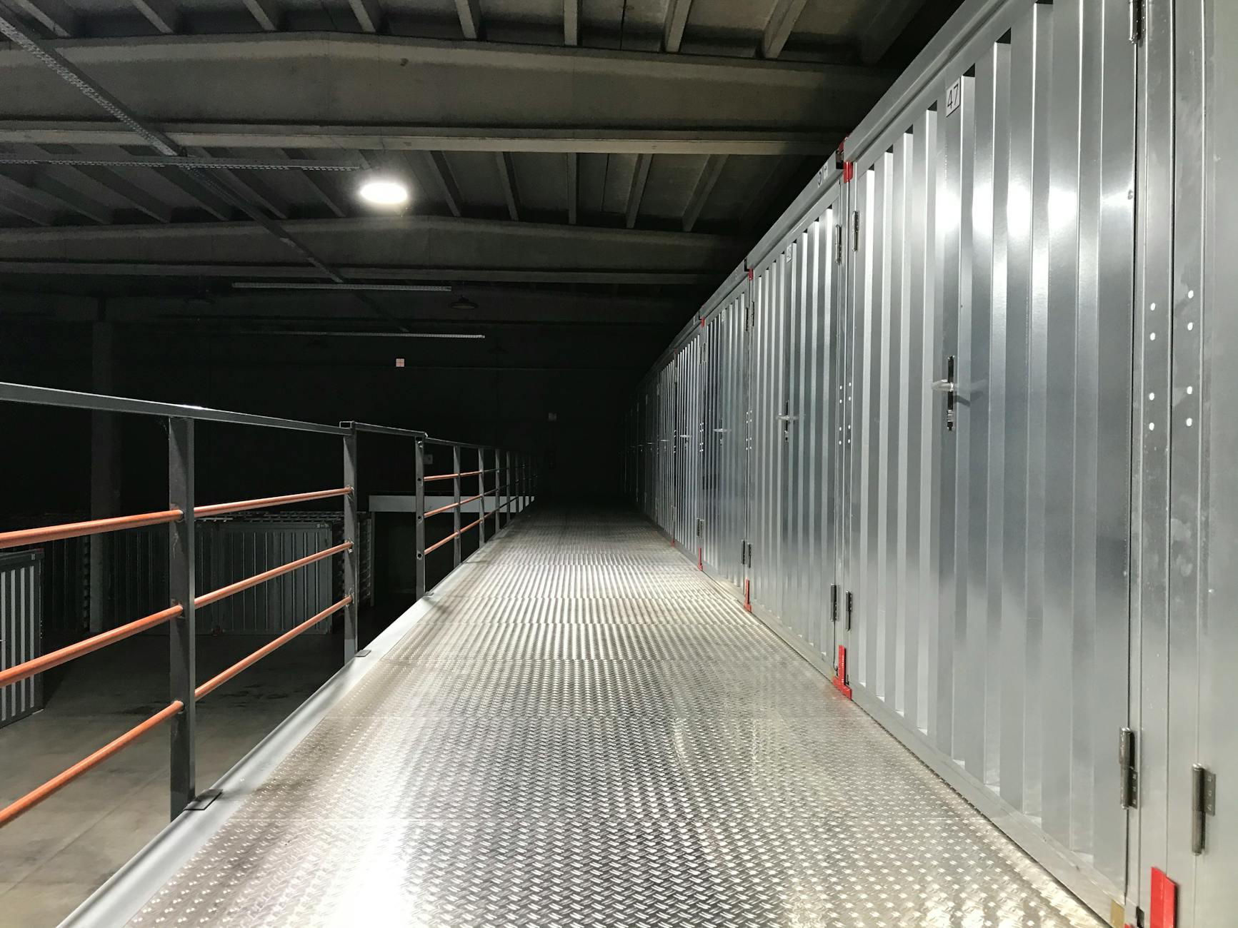 Empty industrial hallway with steel lockers and railing in a warehouse.