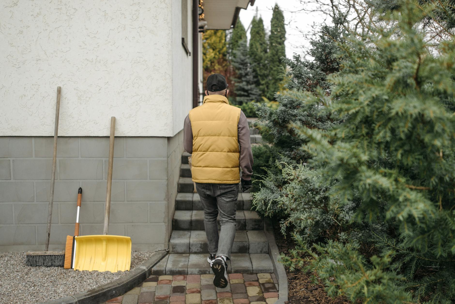 A man in a yellow vest walks towards a house surrounded by greenery.