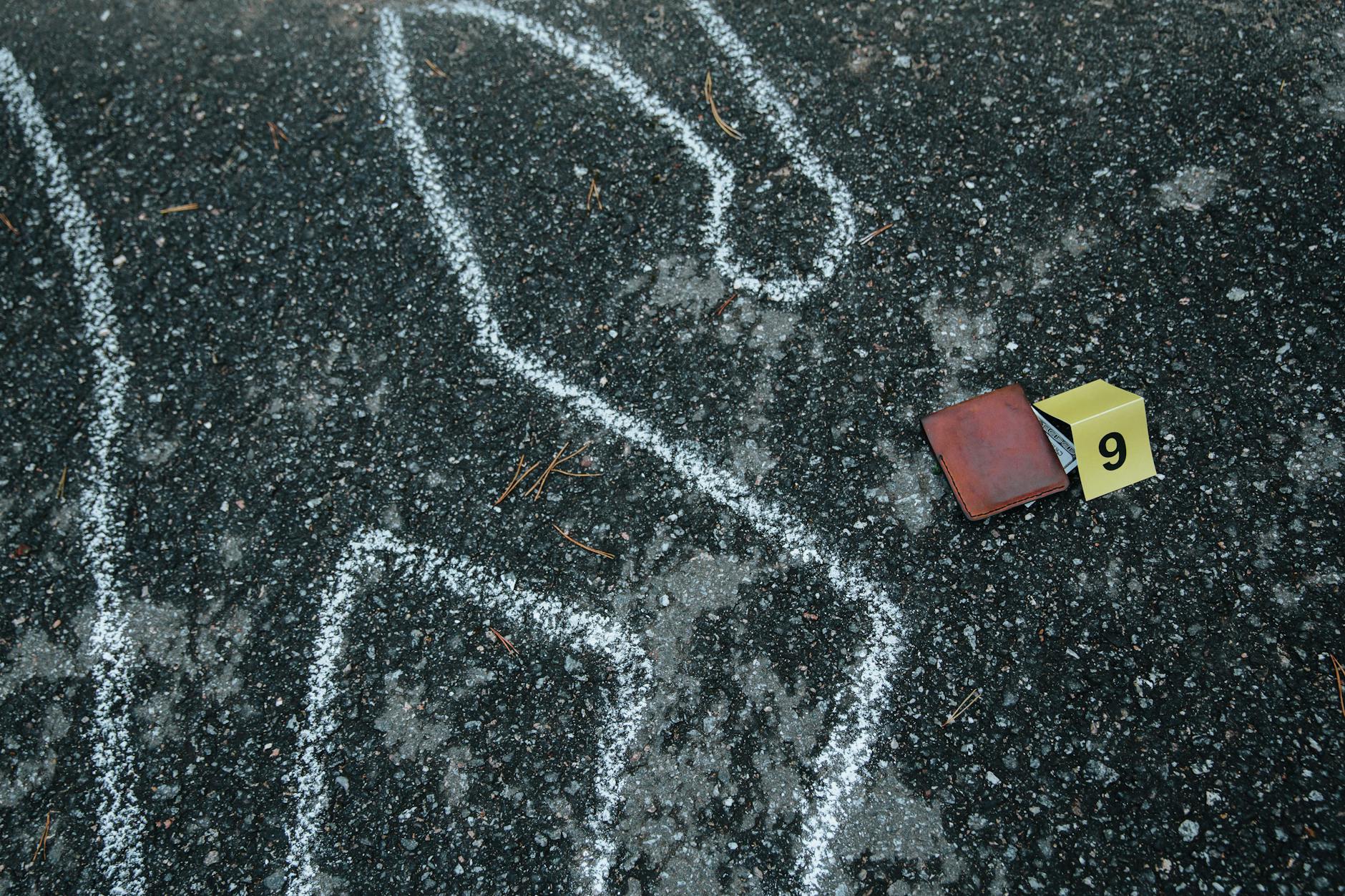 Crime scene with a chalk outline and evidence marker on asphalt.