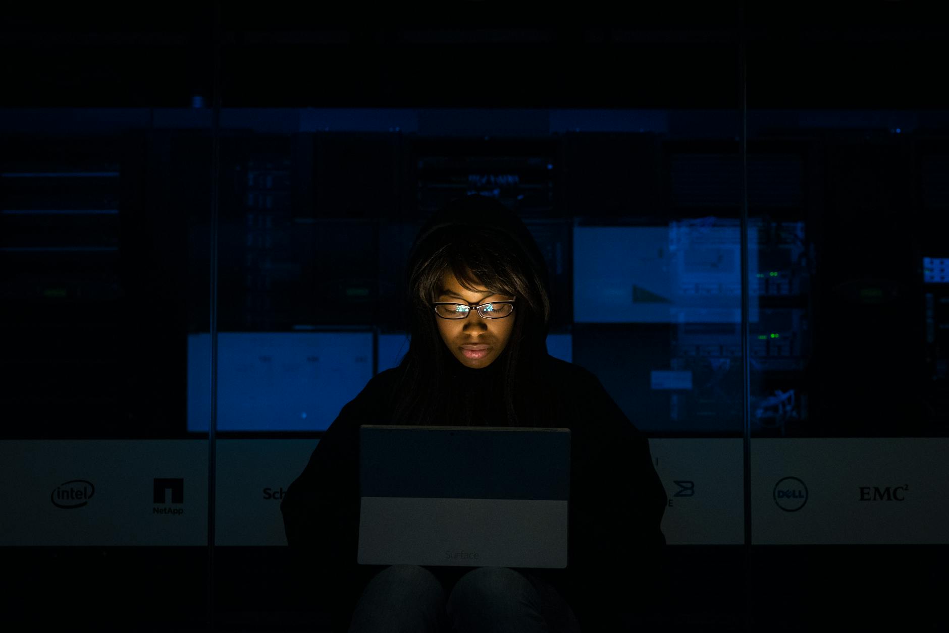 A woman deeply engrossed in programming on a laptop at night in a data center.