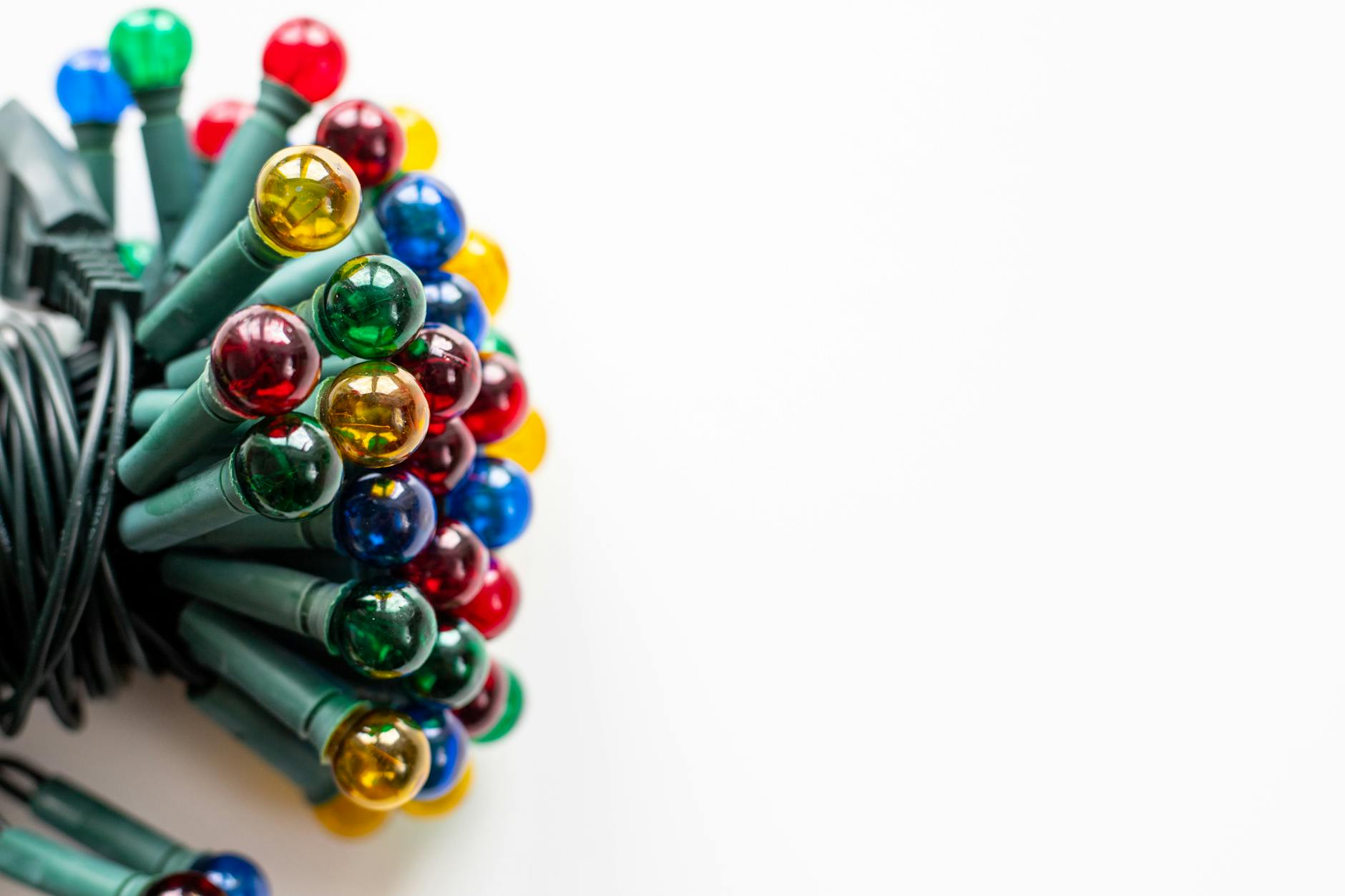 Close-up of colorful Christmas lights with green wire on a white background.