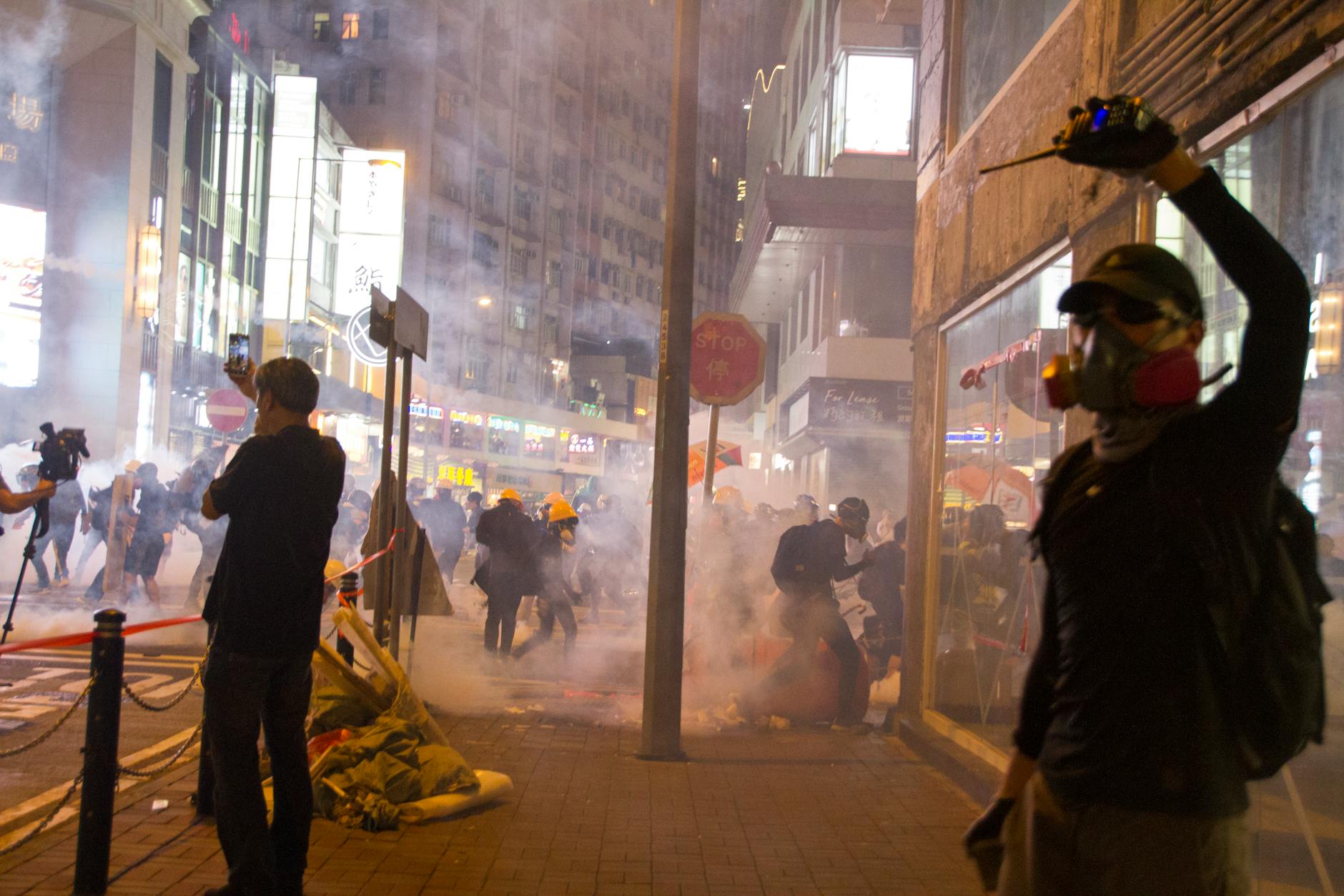 Nighttime street protest scene with smoke and crowd activity in an urban setting.