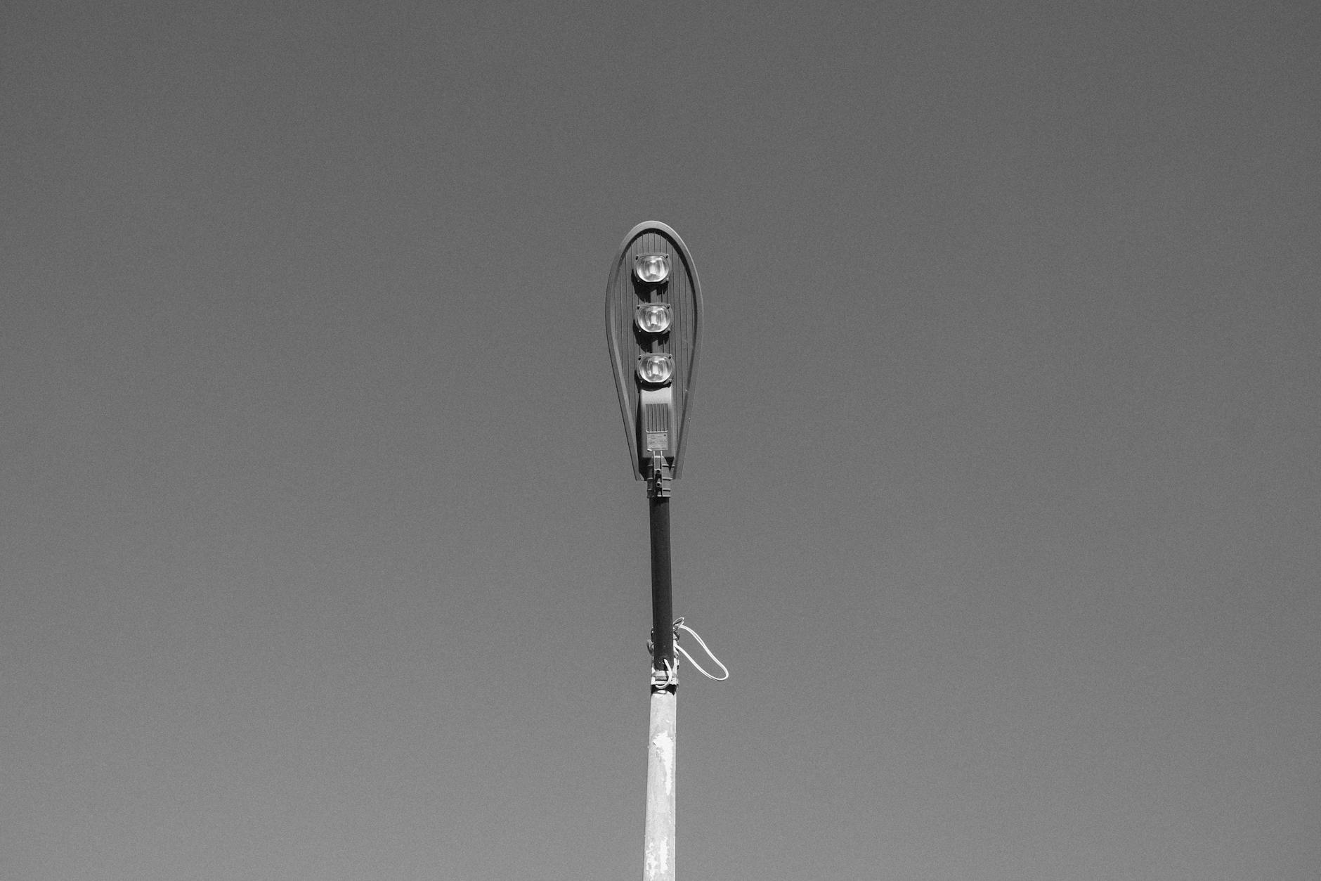 Black and white image of a single streetlight against a clear sky, minimalistic style.