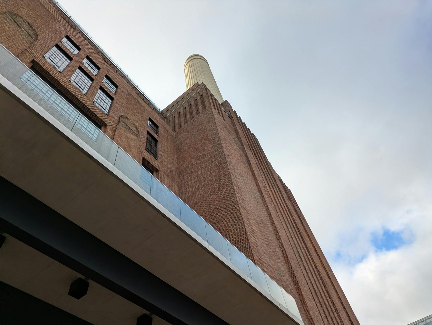 Low-angle view of Battersea Power Station showing its iconic brick chimney against a cloudy sky.