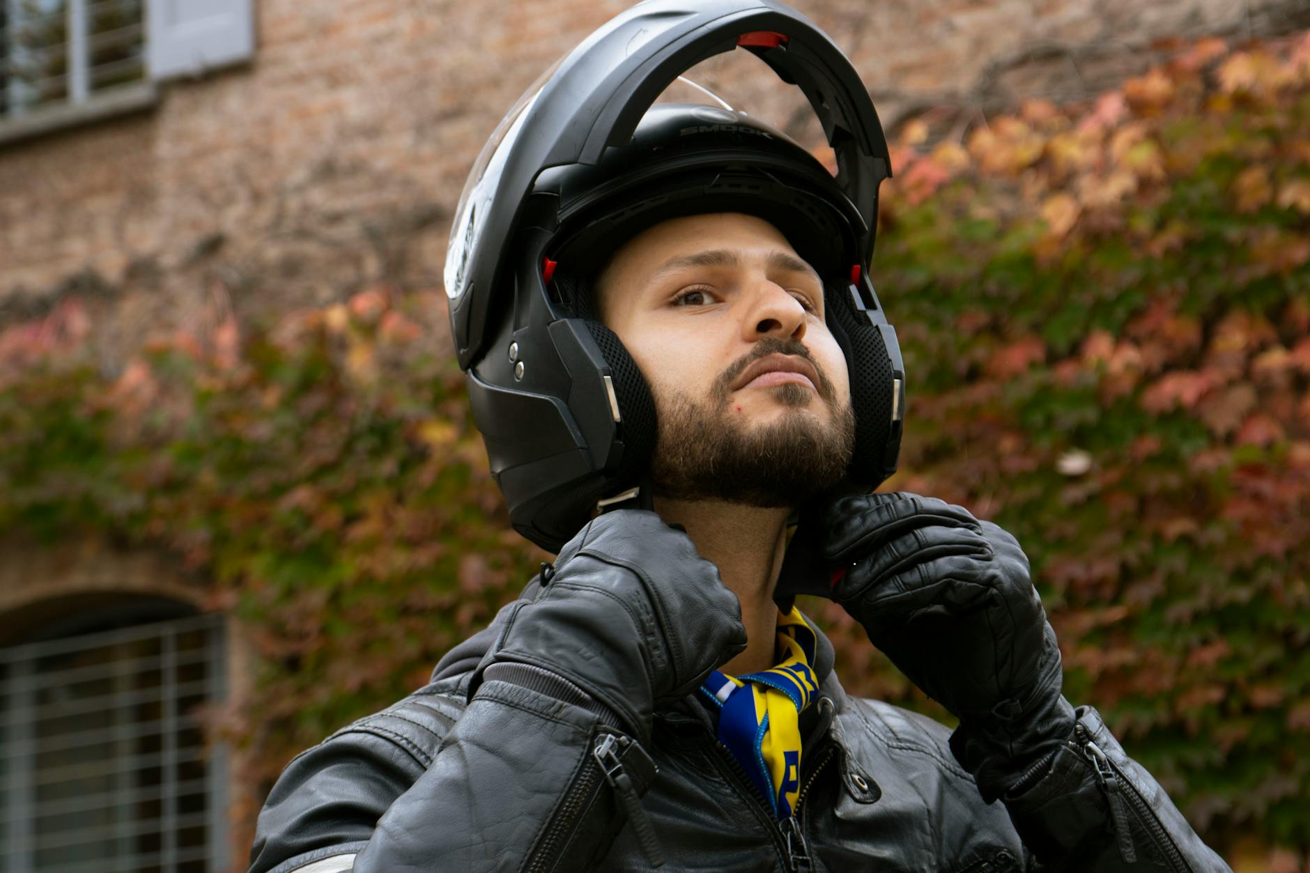 Confident motorcyclist preparing for ride by adjusting helmet on an autumn day in Sassuolo, Italy.
