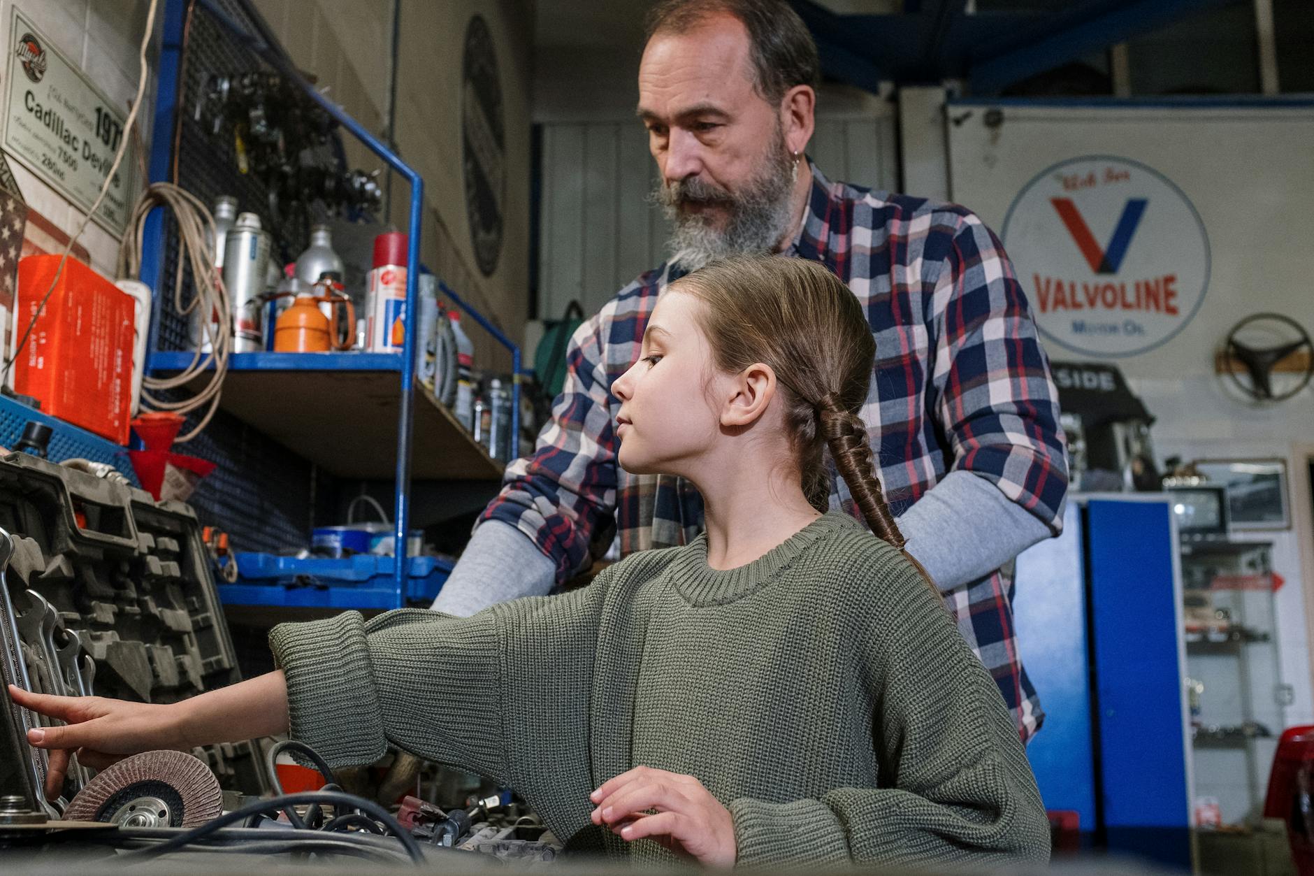 Father and daughter bonding in a garage workshop full of tools and machinery.