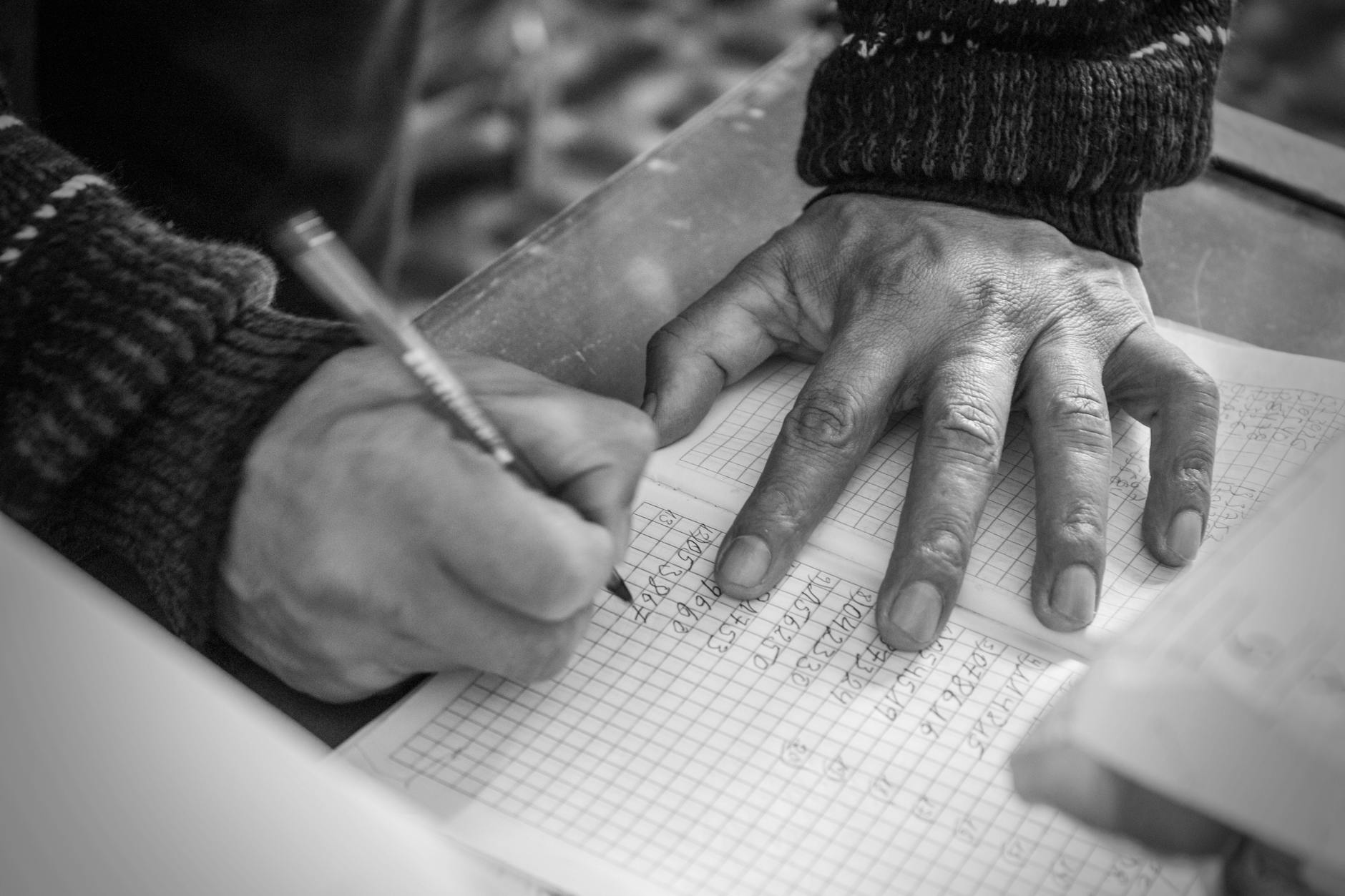 Black and white close-up of a person writing on checkered paper, focusing on hands.