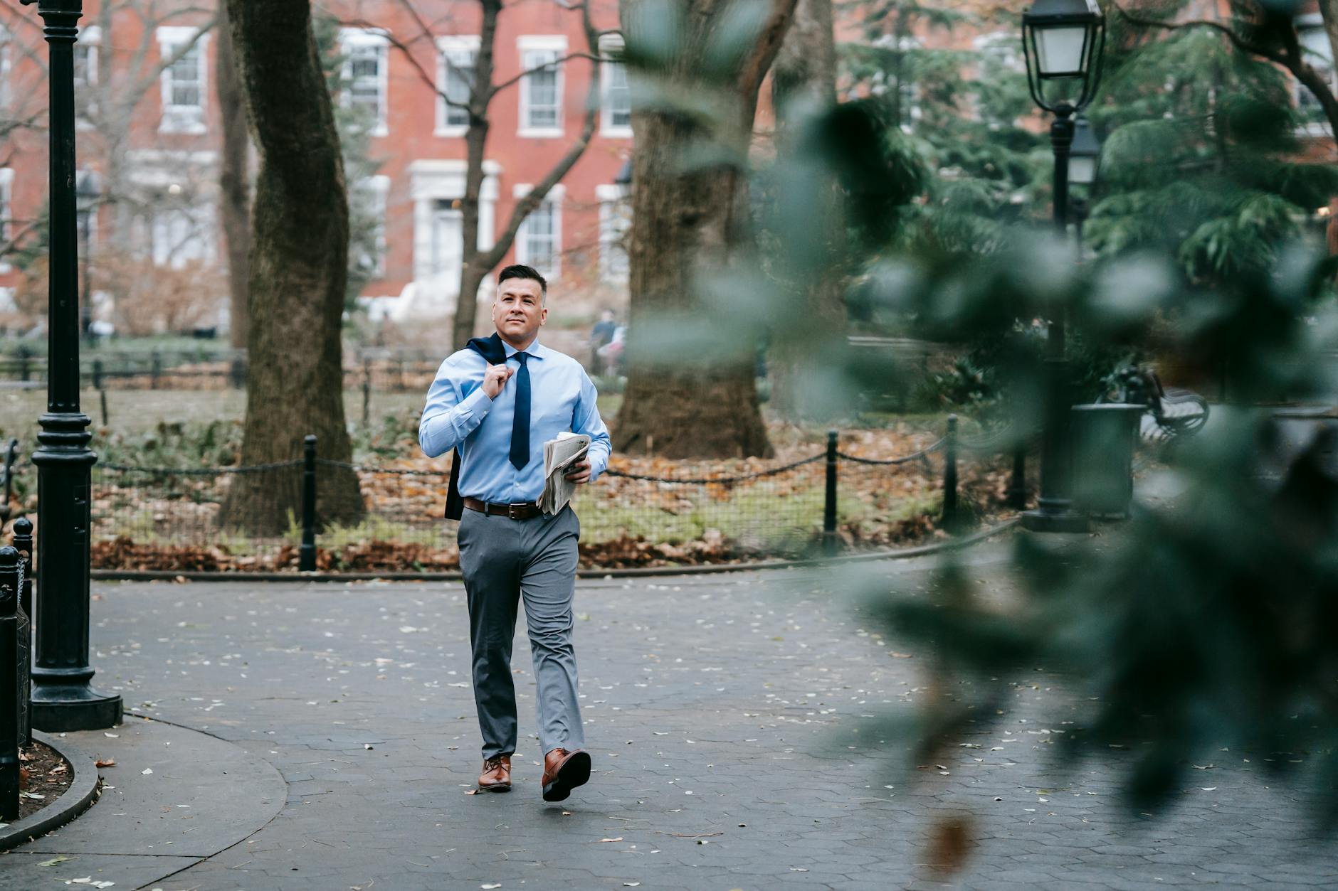 A stylish man in professional attire confidently walks through a serene urban park.
