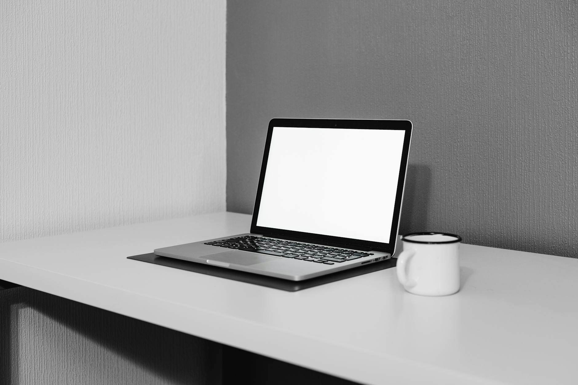 A clean and modern workspace featuring a laptop and white mug on a desk.