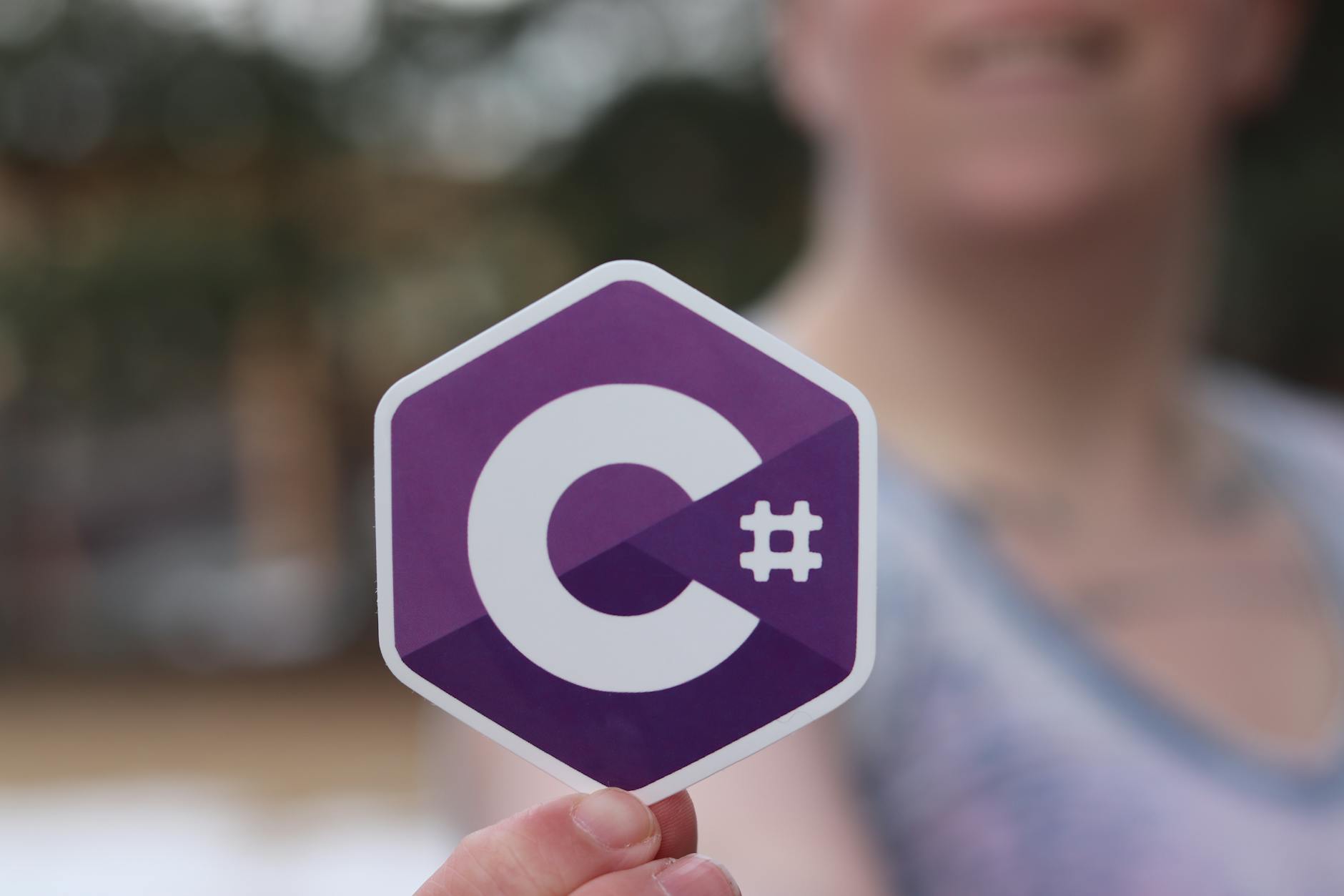 Person holding a C# programming language logo sticker outdoors.