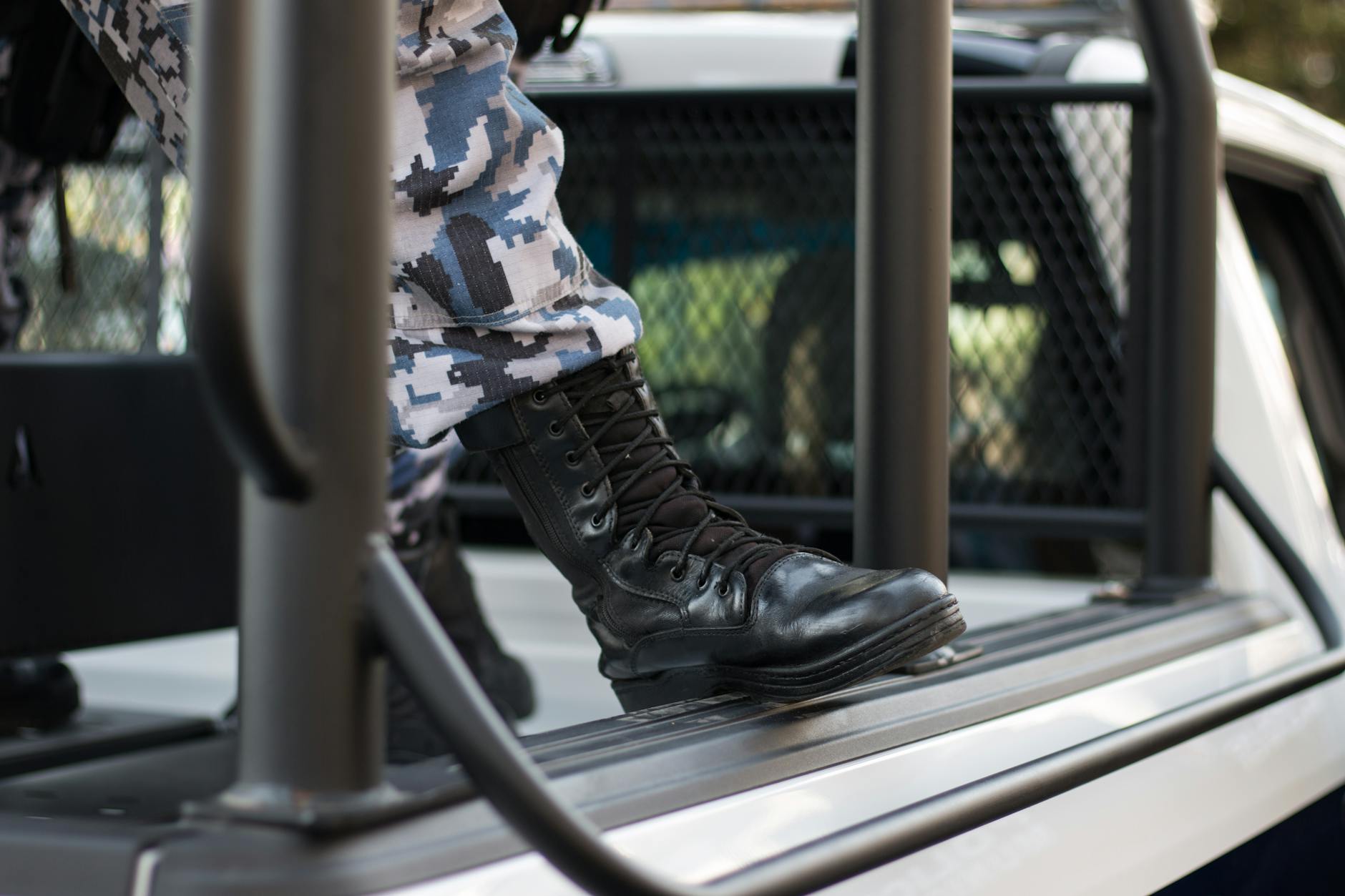 Close-up shot of black boots in camouflage uniform stepping on a police vehicle in Xalapa-Enríquez, Mexico.