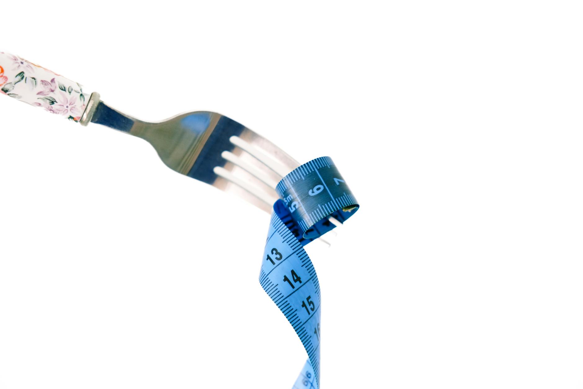 A fork twirls a blue measuring tape, symbolizing weight management and health.