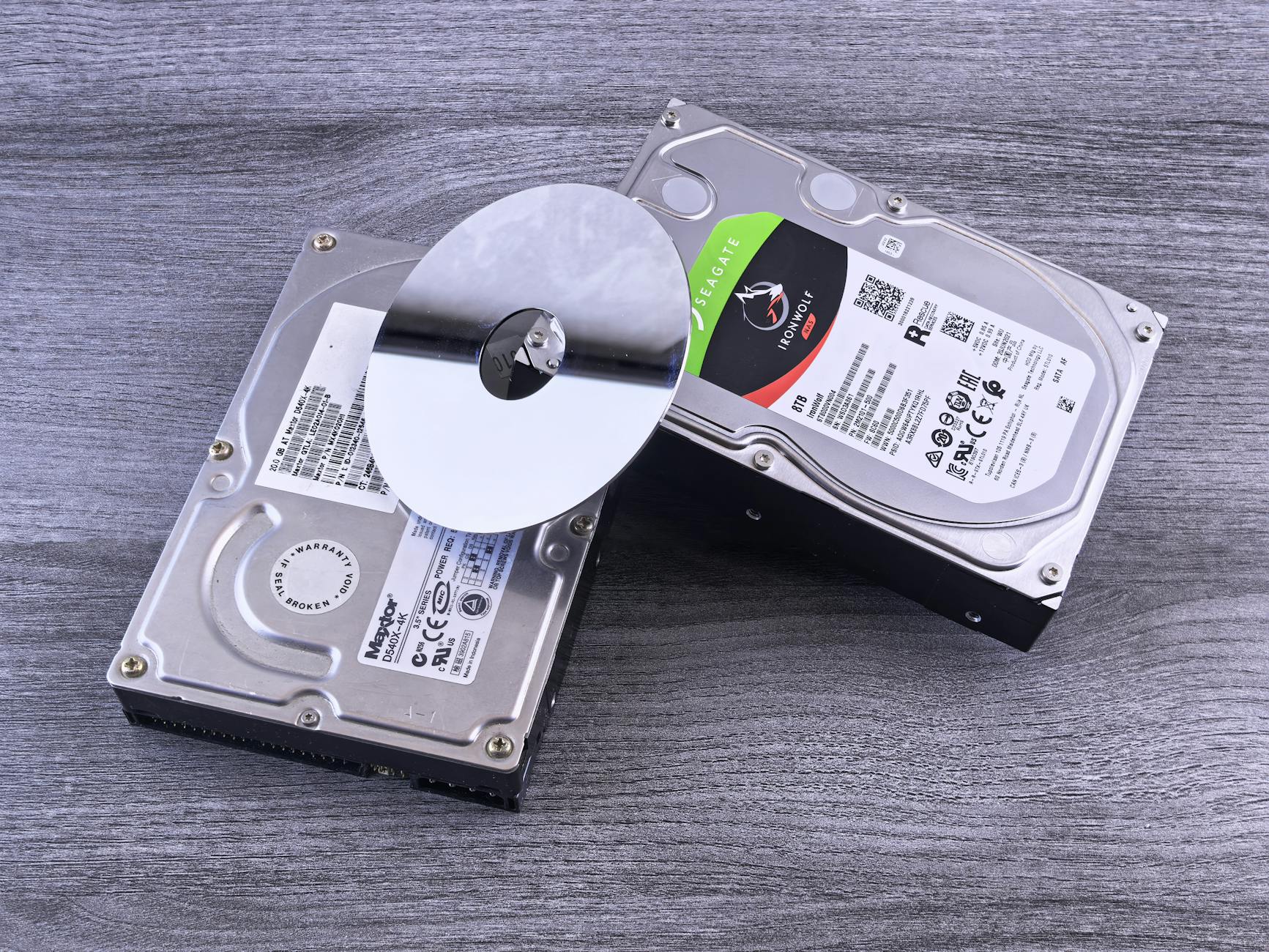 Two computer hard drives and a shiny disk displayed on a wooden surface.