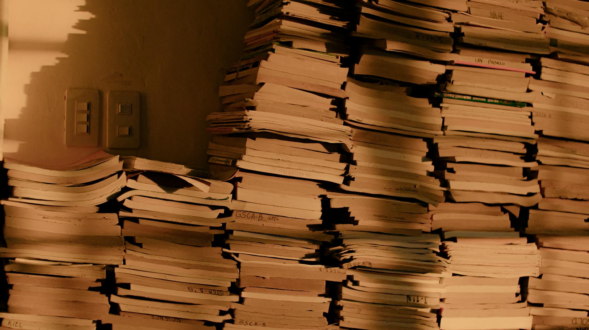 Stacks of old books and papers in shadowy light, suggesting a vintage or historical feel.